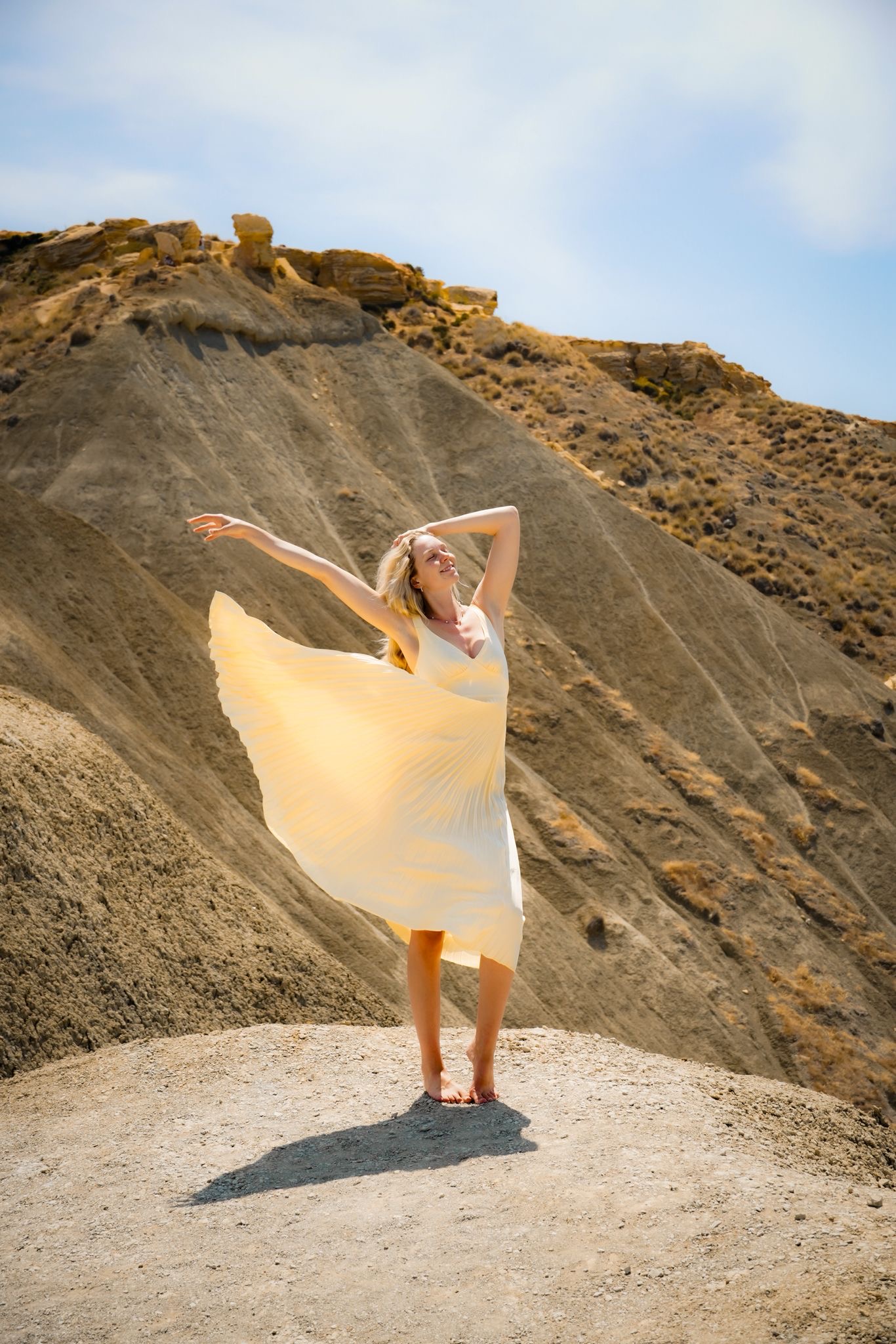 Cece dancing in yellow dress on a sun‑baked hill